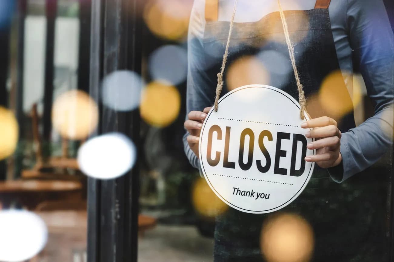 Hand holding CLOSED sign on shop door after hours, highlighting small business call handling challenges.