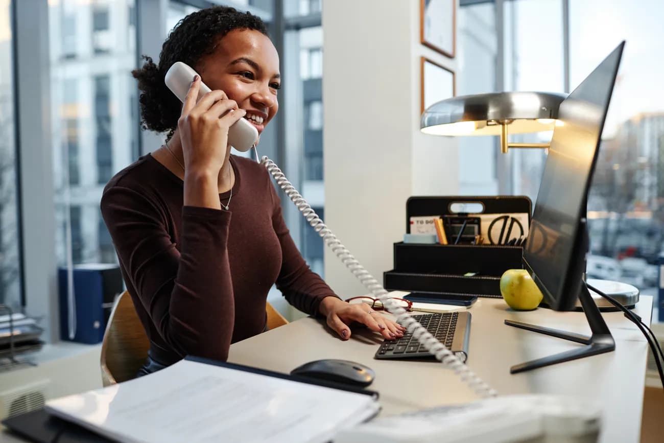 Professional using a classic desk phone in a modern office, highlighting the role of receptionists in business communication.